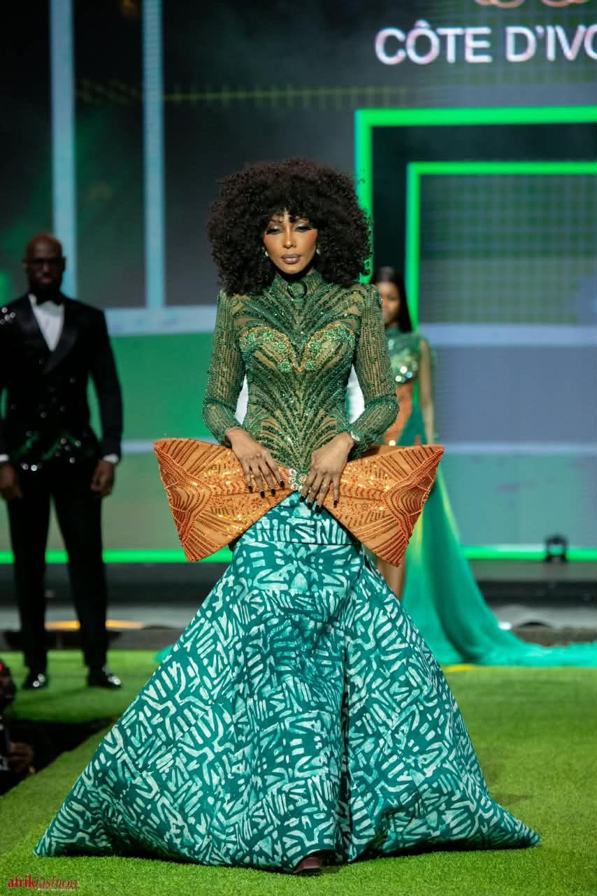 Modèle en robe verte brodée et jupe à motifs sur le podium de l'Afrik Fashion Week