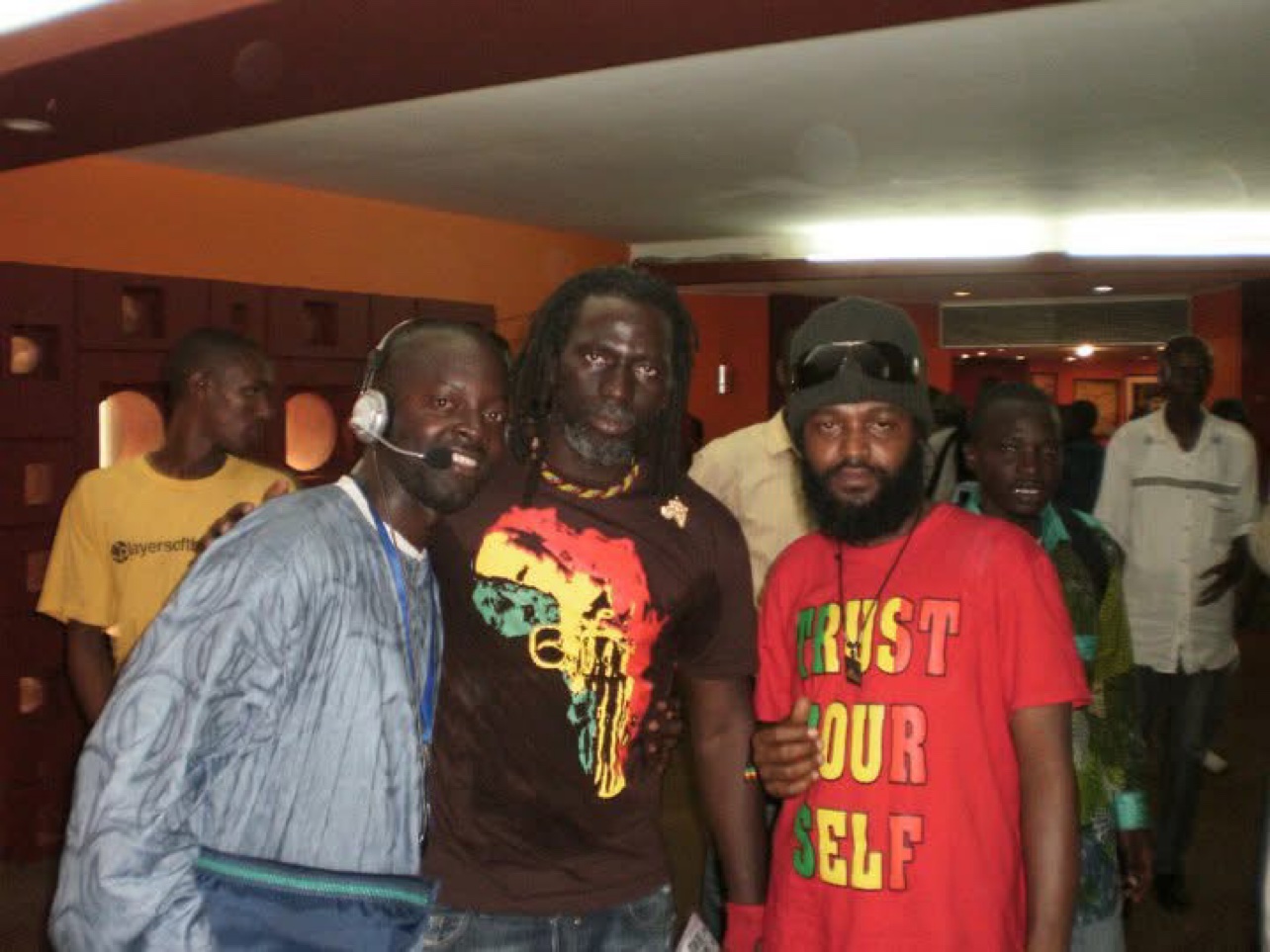 Photo de groupe dans un hall de Conakry : Moïse (à gauche, casque-micro) entouré d'artistes reggae — Projet Tous Ensemble. © Festival TV / Moïse 1er