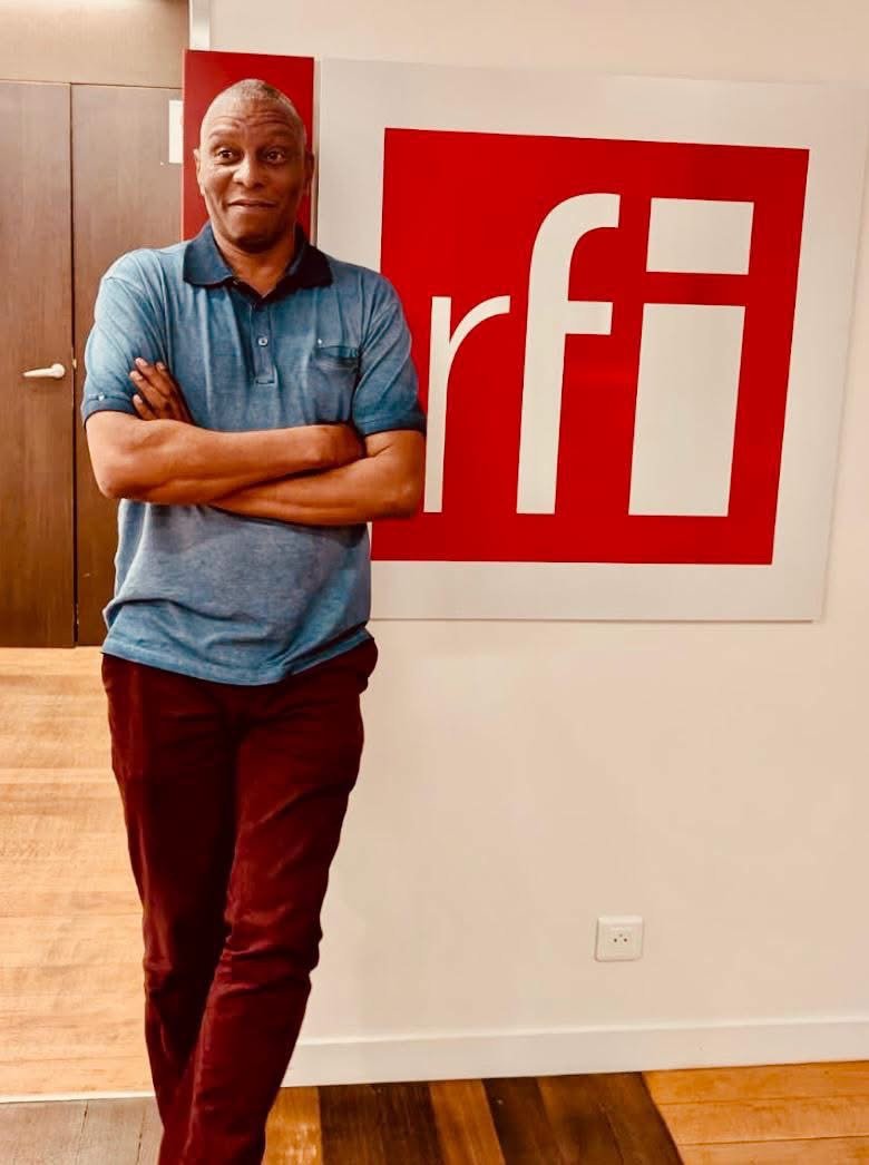 Mory Touré devant le logo de RFI, bras croisés
