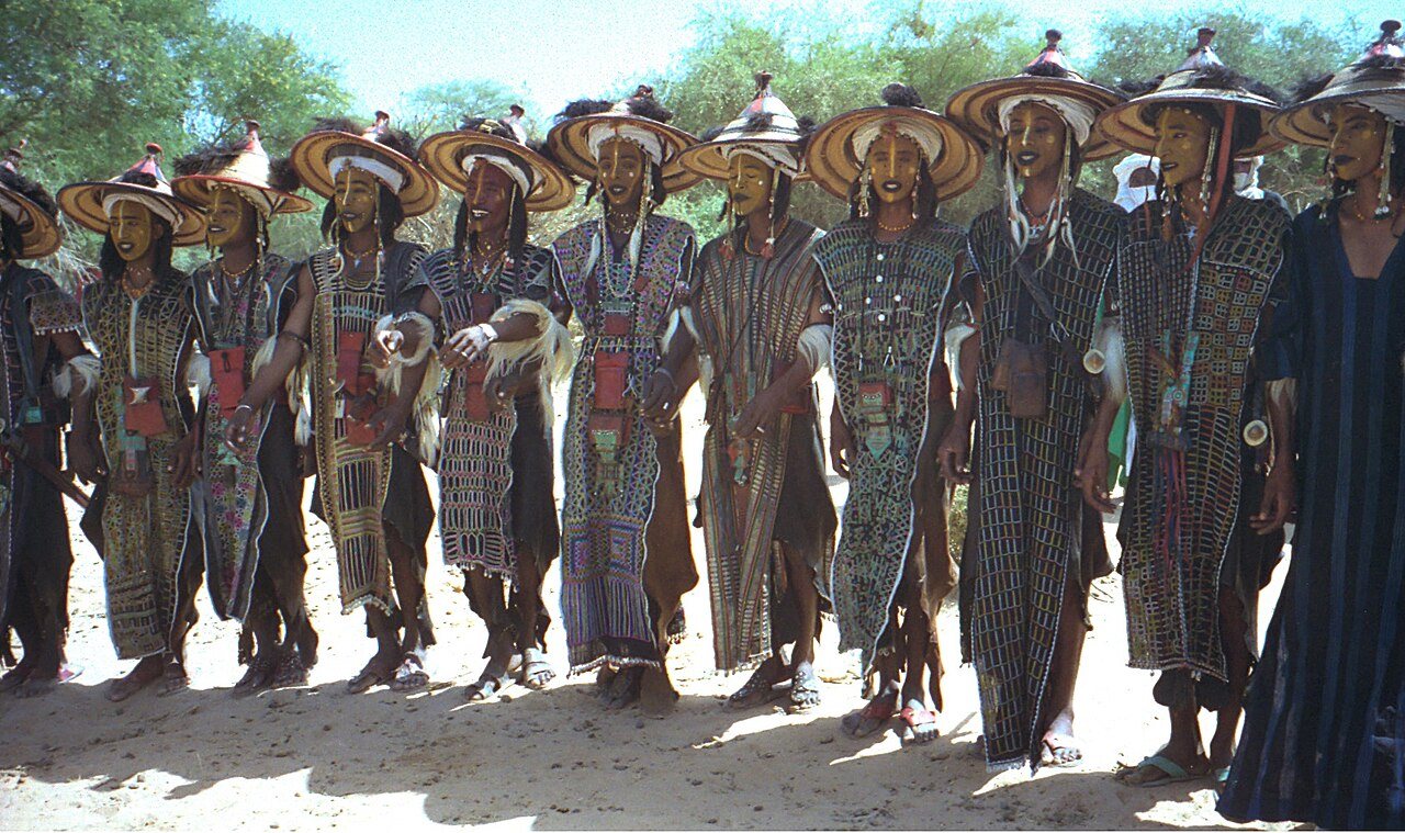 Wudaabe dance line in embroidered tunics and conical hats