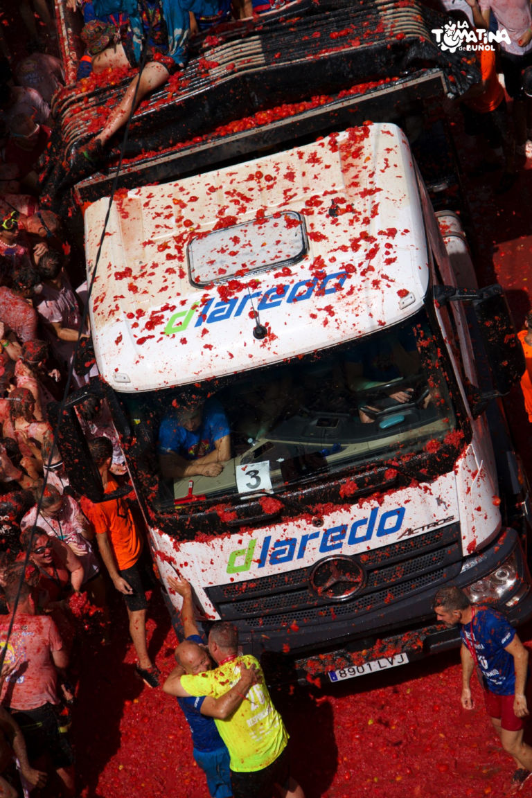 A red-splattered tomato truck crosses the crowd