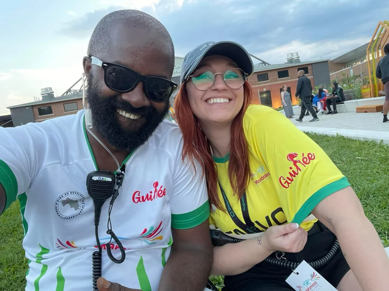 Moïse 1er en maillot de la Guinée, oreillette et radio de régie au cou, en selfie avec une festivalière en maillot jaune du MondoKarnaval, à Montréal