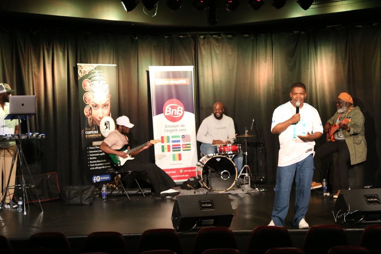 A microphone player in front of the group, between the banners of the partners